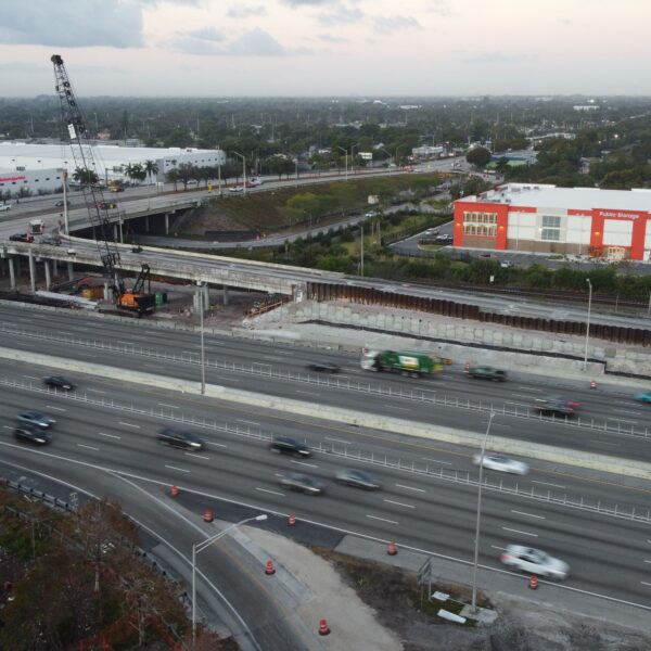 Aerial view of a busy highway interchange with a construction crane and a large Public Storage building on the right.