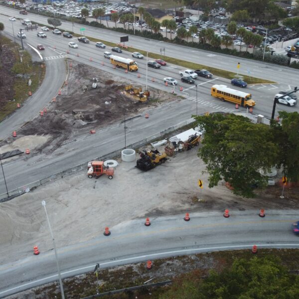 Aerial view of a multi-lane road under construction with orange cones, excavated area, and construction equipment nearby.