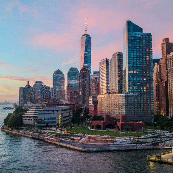 default - Posillico Inc. Sunset skyline of downtown Manhattan with tall skyscrapers along the waterfront and a calm harbor in the foreground.