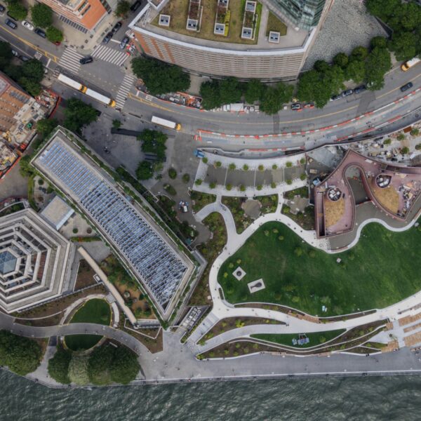Screenshot 2026-10-07 at 14450 PM - Posillico Inc. Aerial view of a riverside urban park with winding paths and green lawns beside a curved promenade along the river edge.